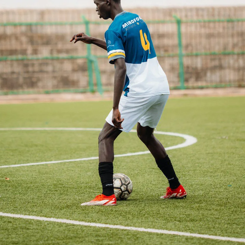 Un footballeur conduit le ballon sur un terrain vert