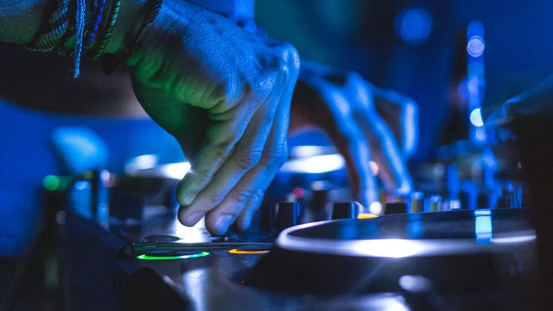 Les mains d'un DJ sur sa console sous une lumière bleue