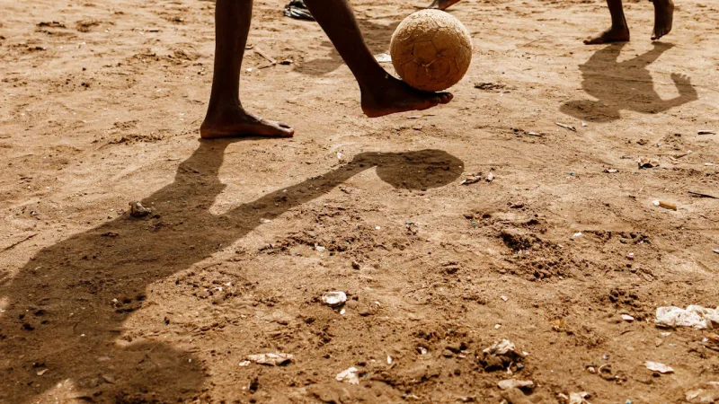 Des jeunes jouent au football sur un terrain de sable