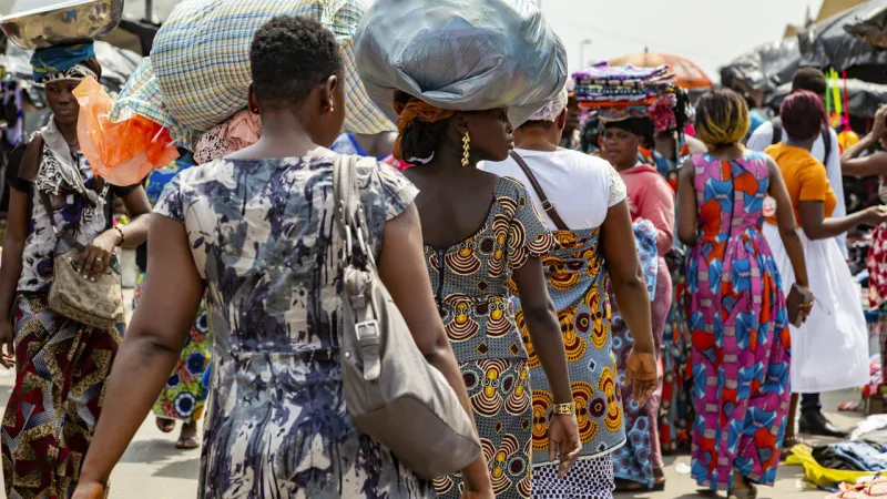 Des femmes en pagne marchent dans une rue animée de marché