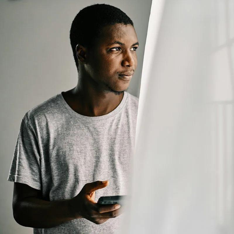 Un jeune homme, smartphone à la main, près d'une fenêtre
